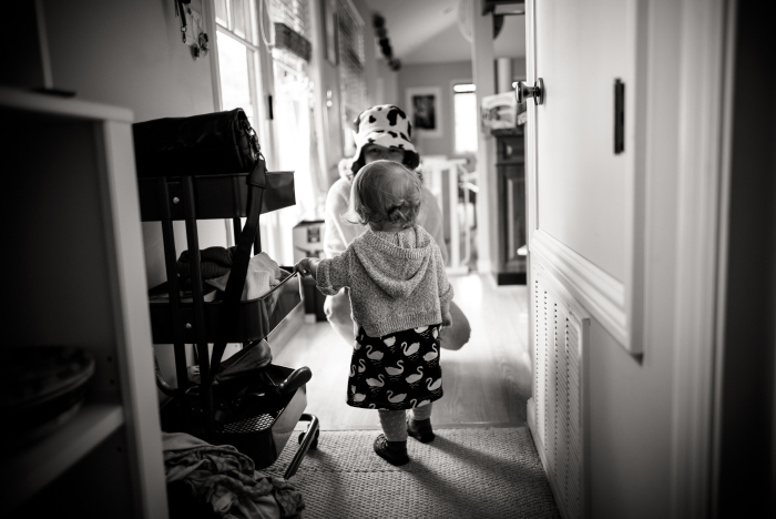 Un bébé tourne le dos à l'appareil photo dans le couloir de sa maison. 